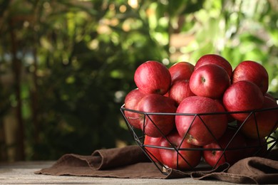 Ripe red apples in bowl on wooden table outdoors, space for text