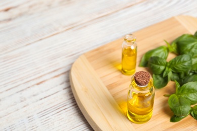 Photo of Wooden board with glass bottles of basil oil,leaves and space for text