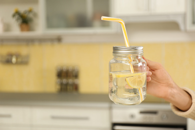 Photo of Young woman with mason jar of lemon water in kitchen, closeup. Space for text