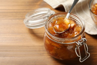 Photo of Tasty apple jam and spoon in glass jar on wooden table, closeup. Space for text