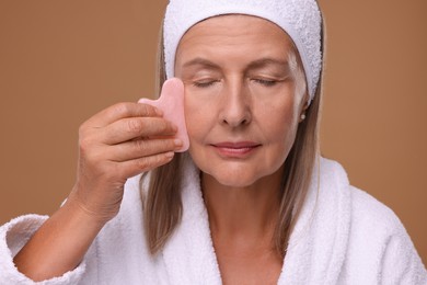 Photo of Woman massaging her face with rose quartz gua sha tool on brown background