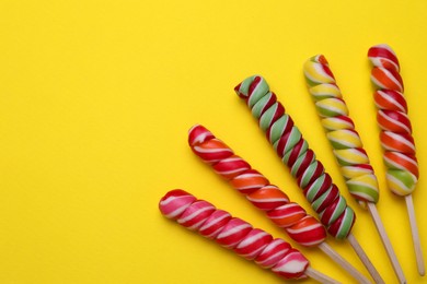 Photo of Delicious lollipops on yellow background, flat lay. Space for text