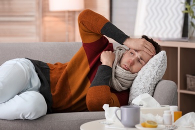 Photo of Sick young man with headache suffering from cold on sofa at home