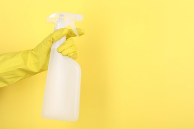 Photo of Woman holding plastic spray bottle on yellow background, closeup. Space for text
