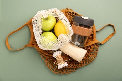 Photo of Fishnet bag with different items on pale green background, top view. Conscious consumption
