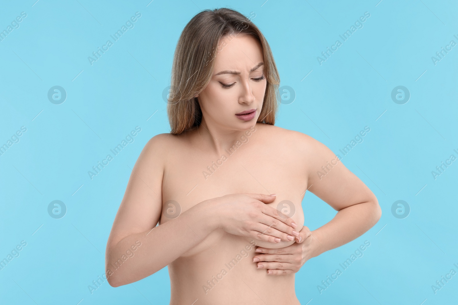 Photo of Mammology. Naked young woman doing breast self-examination on light blue background