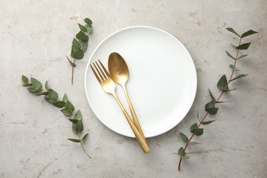Photo of Stylish setting with cutlery, eucalyptus branches and plate on light grey table, flat lay