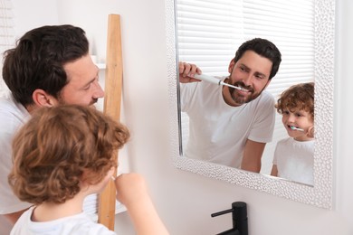 Photo of Father and his son brushing teeth together near mirror in bathroom