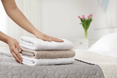Photo of Young maid putting stack of fresh towels on bed in hotel room, closeup