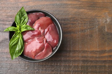 Photo of Bowl of raw chicken liver with basil on wooden table, top view. Space for text