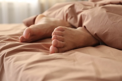 Photo of Person in bed with brown linens at home, closeup on feet