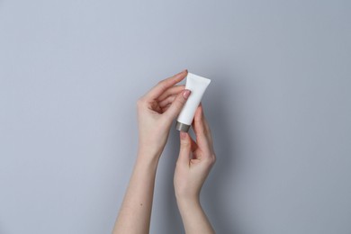 Photo of Woman holding tube of cream on grey background, closeup