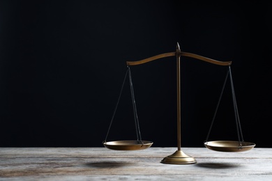 Photo of Scales of justice on wooden table against dark background. Law concept