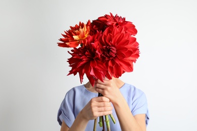 Photo of Woman holding bouquet of beautiful dahlia flowers against light background
