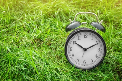 Photo of Alarm clock on green grass, outdoors. Time change concept