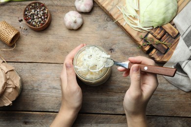 Photo of Woman eating fermented cabbage at wooden table, top view