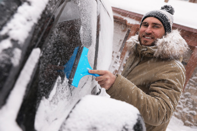 Photo of Young man cleaning snow from car window outdoors on winter day