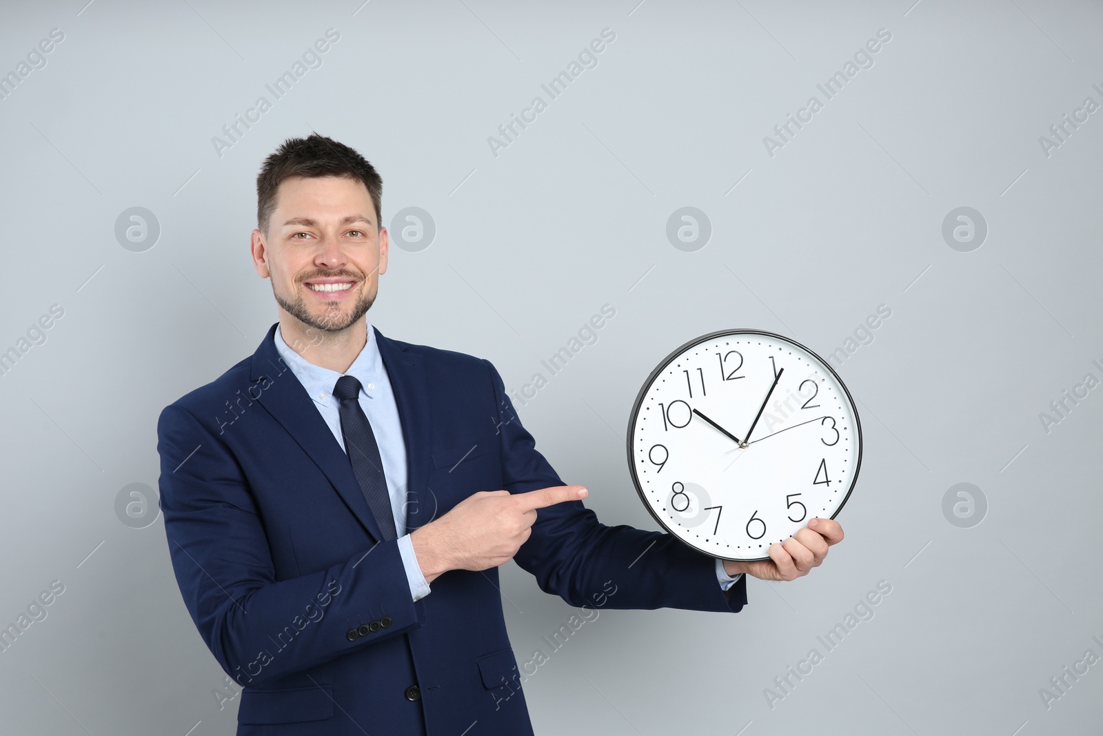 Photo of Happy businessman holding clock on grey background. Time management