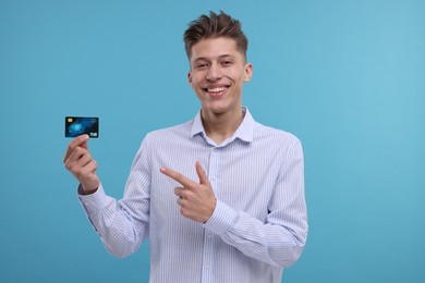 Photo of Happy man pointing at credit card on light blue background