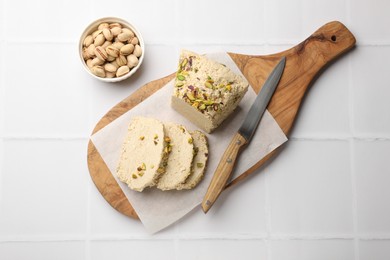 Photo of Tasty halva with pistachios and knife on white tiled table, top view
