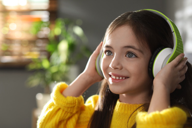 Photo of Cute little girl with headphones listening to audiobook at home