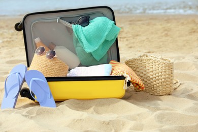 Photo of Open suitcase with beach items on sandy seashore