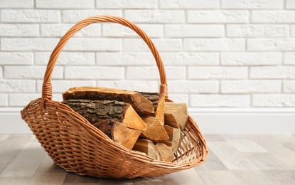 Photo of Wicker basket with firewood near white brick wall indoors, space for text