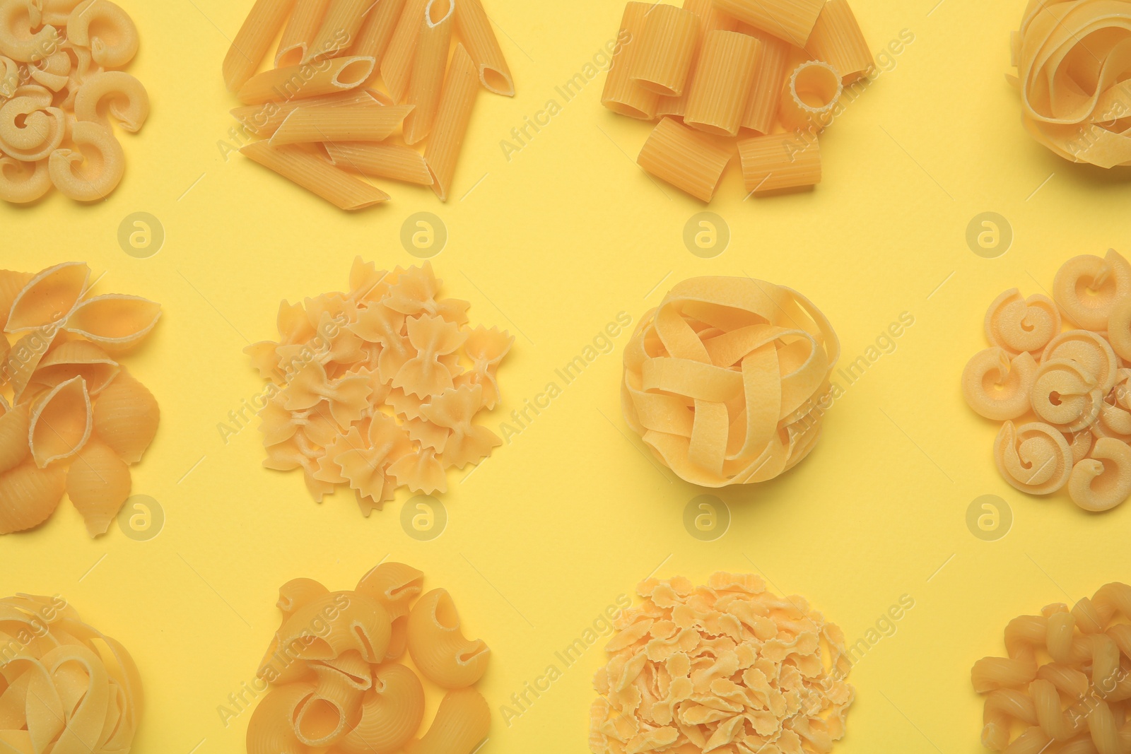 Photo of Different types of pasta on yellow background, flat lay