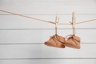 Photo of Cute baby shoes drying on washing line against white wall. Space for text
