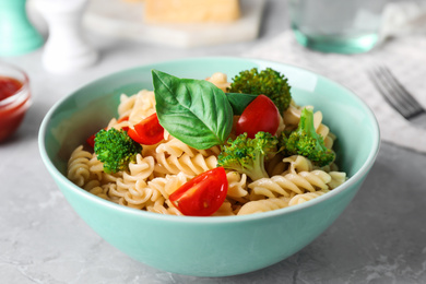 Photo of Tasty pasta with broccoli, cherry tomatoes and basil on light grey marble table, closeup