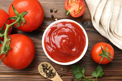 Photo of Delicious ketchup in bowl, tomatoes and peppercorns on wooden table, flat lay