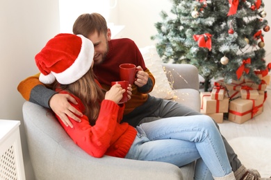 Photo of Happy young couple with cups of hot drink celebrating Christmas at home