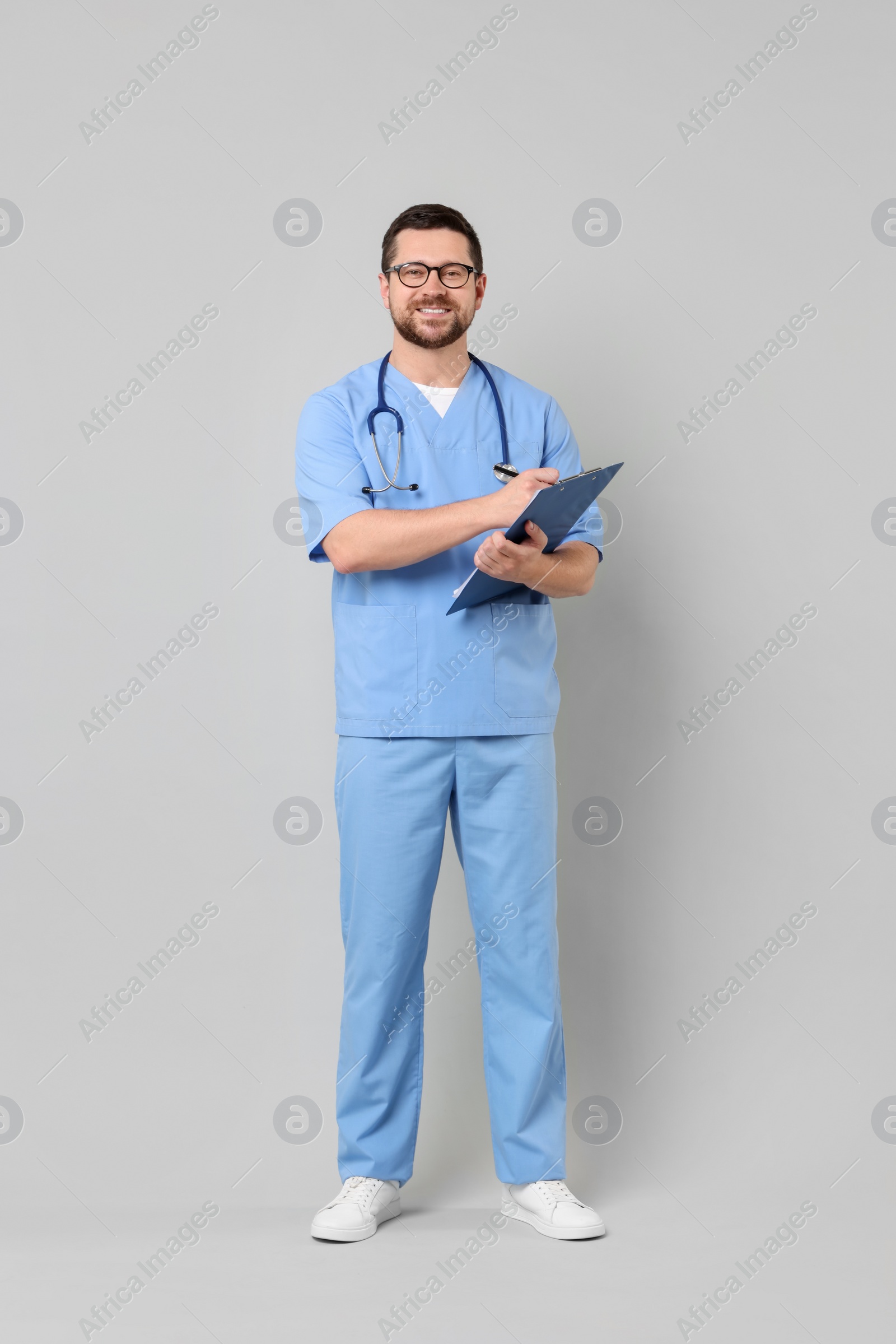 Photo of Smiling doctor with clipboard on light grey background