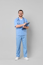 Photo of Smiling doctor with clipboard on light grey background