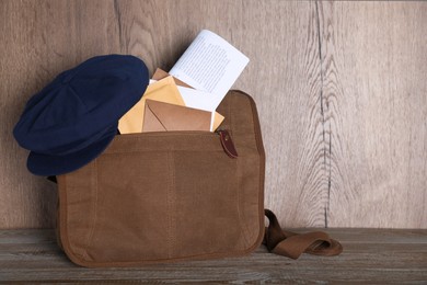 Photo of Postman's hat on bag full of letters and newspapers on wooden background. Space for text