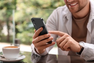 Photo of Man typing message on smartphone at table in outdoor cafe, closeup