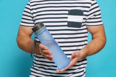 Photo of Man holding transparent plastic bottle of water on light blue background, closeup