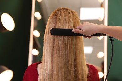 Stylist straightening woman's hair with flat iron in salon