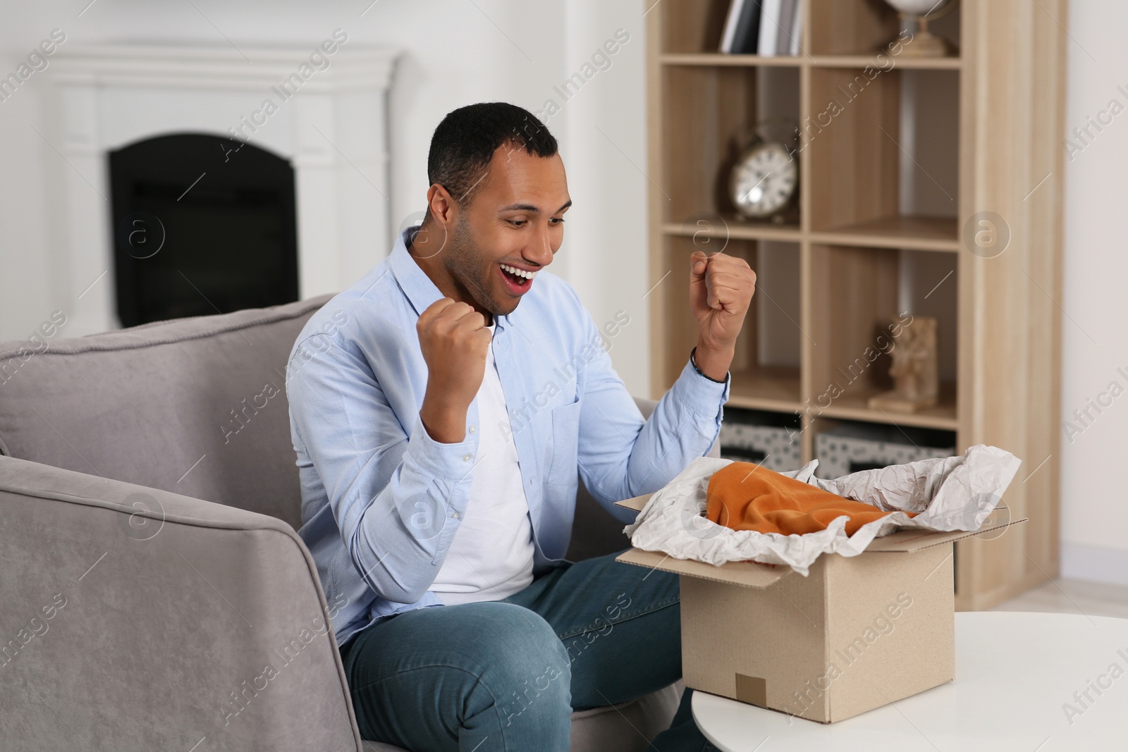 Photo of Happy young man opening parcel at home. Internet shopping