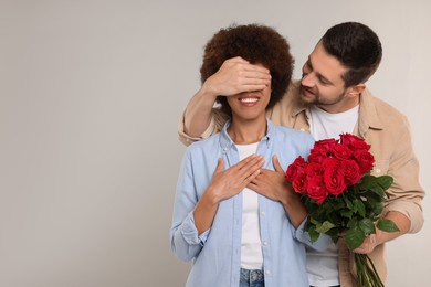 Photo of International dating. Handsome man presenting roses to his beloved woman on light grey background, space for text