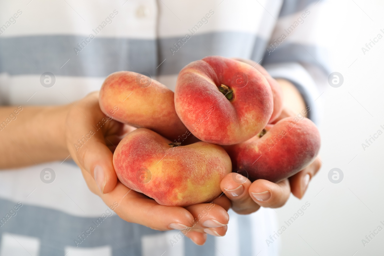 Photo of Woman holding heap of fresh ripe donut peaches on light background, closeup