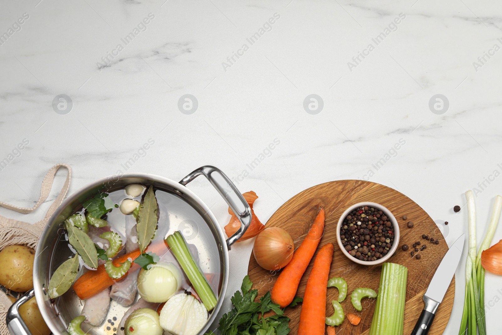 Photo of Pot and different ingredients for cooking tasty bouillon on white marble table, flat lay. Space for text