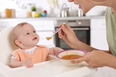 Photo of Woman feeding her child in highchair indoors. Healthy baby food