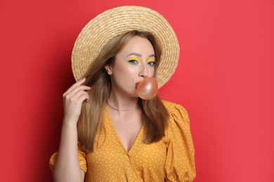 Photo of Fashionable young woman with bright makeup blowing bubblegum on red background