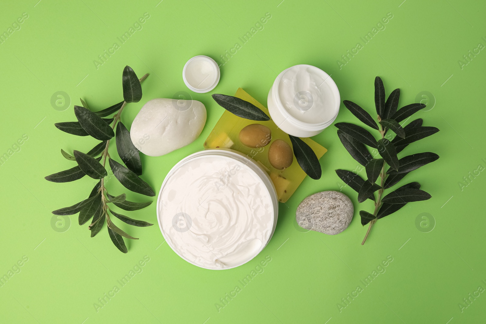 Photo of Different cosmetic products with olives and stones on light green background, flat lay