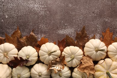 Ripe white pumpkins and dry leaves on grey textured table, flat lay. Space for text