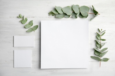 Fresh eucalyptus leaves and blank cards with space for design on wooden background, top view