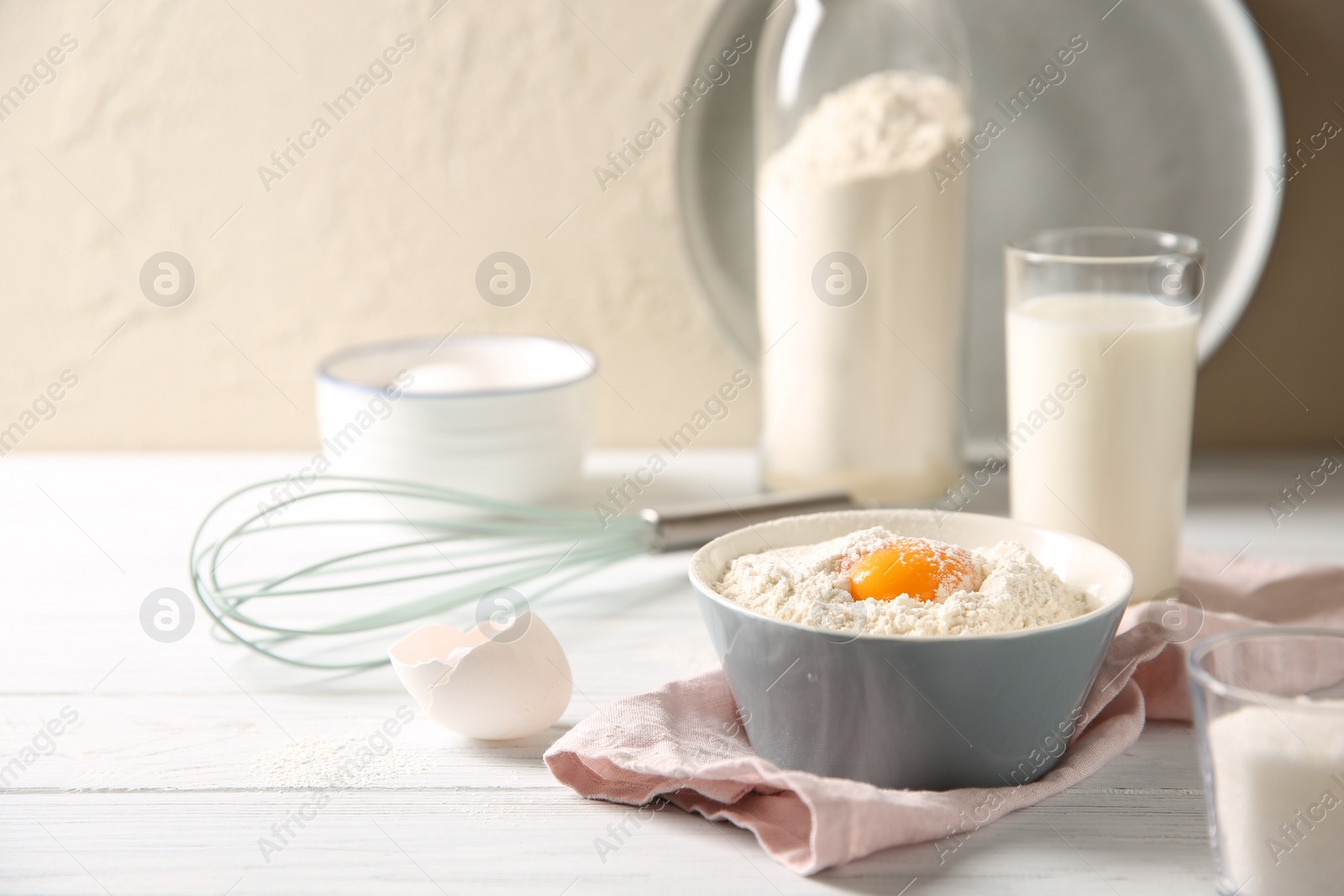 Photo of Making dough. Flour with yolk in bowl on white wooden table. Space for text