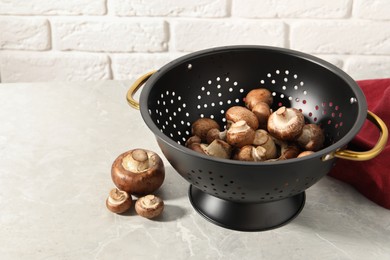 Photo of Raw mushrooms in black colander on marble table. Space for text