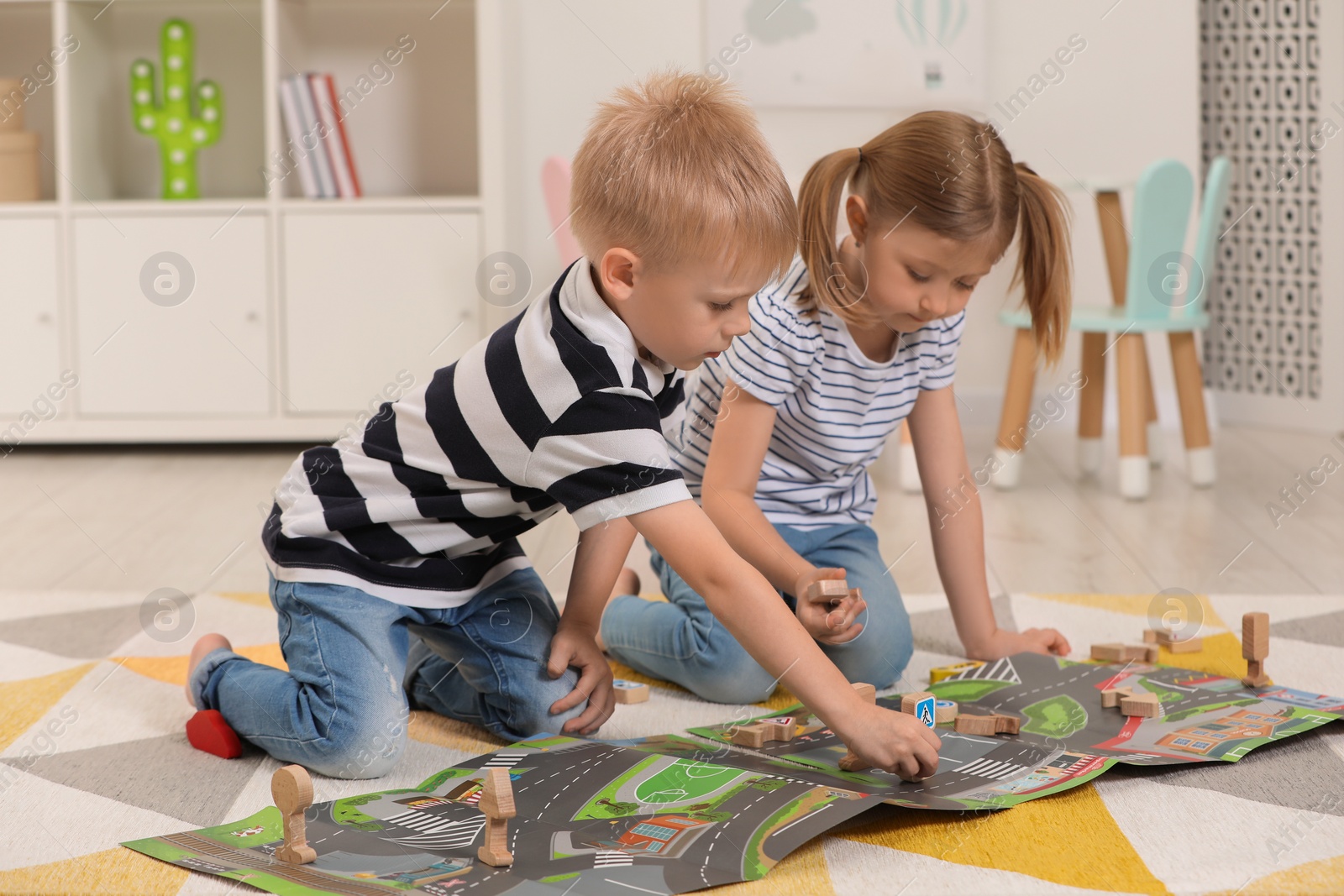 Photo of Little children playing with set of wooden road signs and toy cars indoors